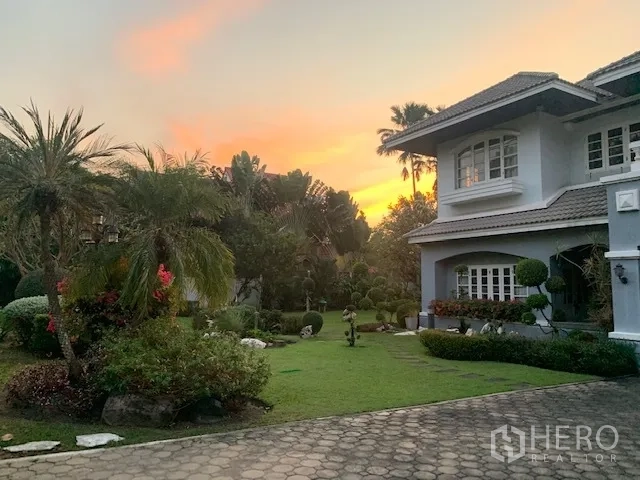 Detached House for rent in Khan Na Yao, Bangkok - Lush landscaped garden at sunset with palms, manicured lawn, and stone path beside the house.