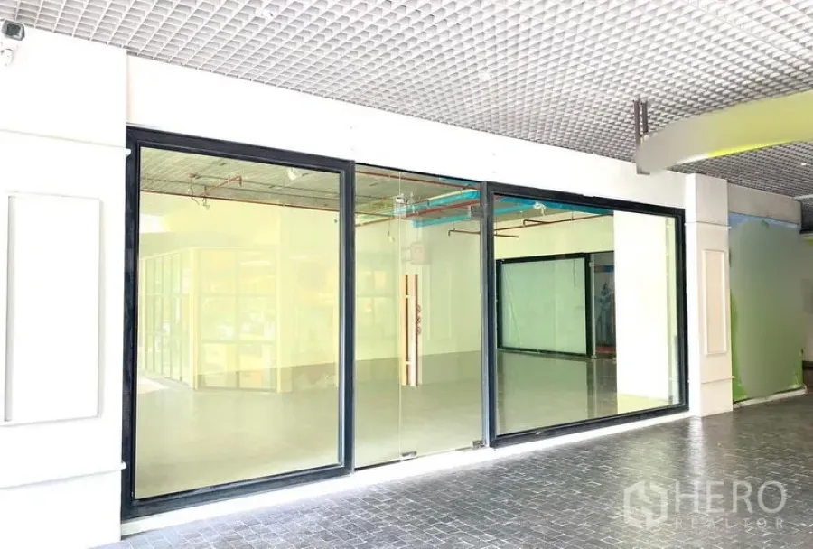 Retail Space for rent in Khlong Toei, Bangkok - Wide glass storefront with black frames and a clear entrance door along an indoor corridor.