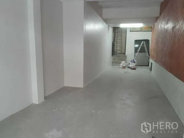 Retail Space for rent in Watthana, Bangkok - Long unfurnished retail unit with white walls, grey floor and ceiling light, rear access and renovation tools visible.