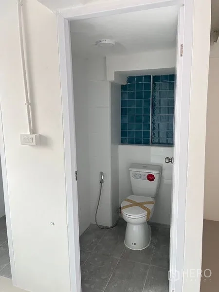 Retail Space for rent - Compact restroom with toilet, handheld bidet, and blue tile accent wall.
