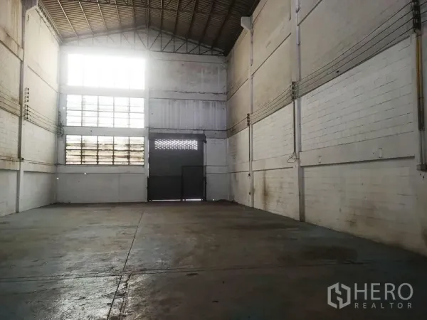 Factory for sale in Khlong Luang, Pathum Thani - High-ceiling warehouse with clerestory windows, concrete floor and roller shutter door.