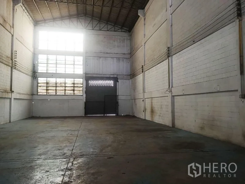 Factory for sale in Khlong Luang, Pathum Thani - High-ceiling warehouse with clerestory windows, concrete floor and roller shutter door.