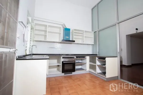Townhouse for rent in Khlong Toei, Bangkok - Bright L-shaped kitchen with white cabinetry, built-in oven, and frosted glass partition.