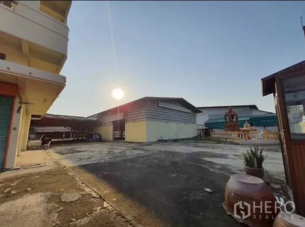 货栈 出租或出售在Mueang Pathum Thani, Pathum Thani - 宽阔硬化院场对向多座仓库，夕阳下并有小神龛。