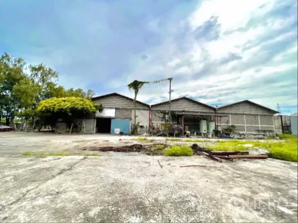 Factory for rent in Sai Noi, Nonthaburi - Front elevation of factory buildings facing an open loading yard with greenery.
