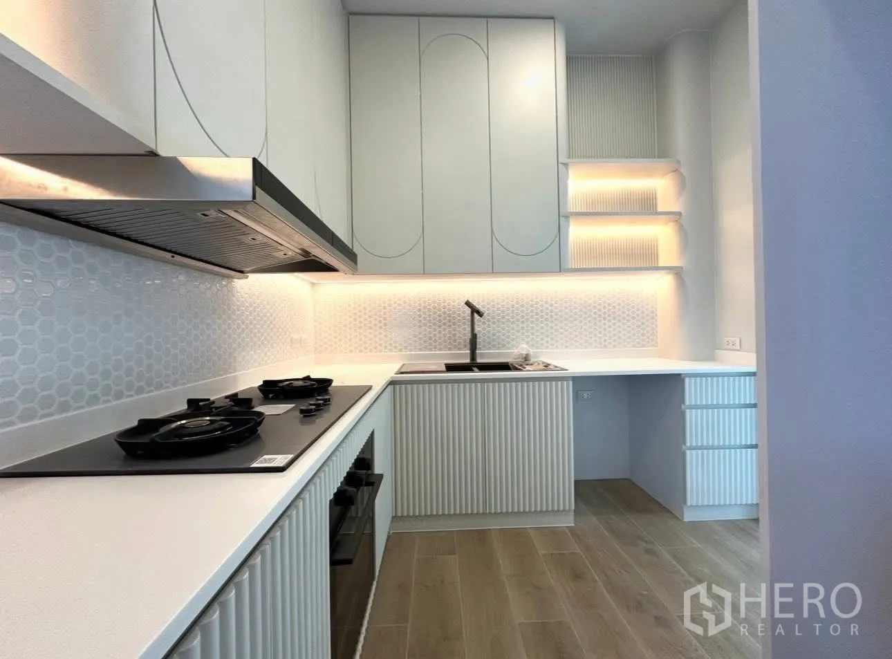 Detached House for sale in Bang Khen, Bangkok - Sleek built-in kitchen with gas hob, hood, white counters and illuminated shelves.