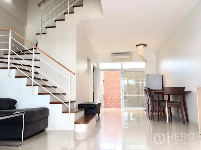 Townhouse for rent in Prawet, Bangkok - An open-plan living and dining area with glossy floors and a modern staircase.