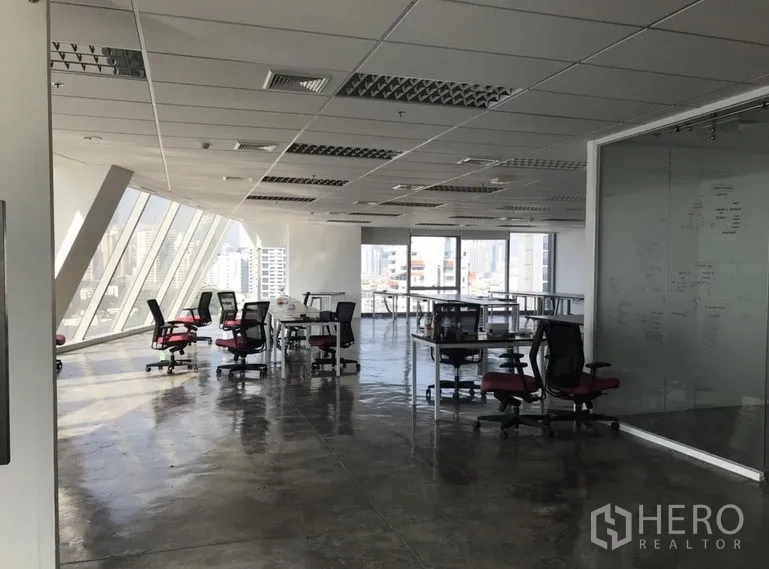 Office Space for rent in Khlong Toei, Bangkok - Open‑plan office with angled floor‑to‑ceiling windows, city views, polished concrete floors and a glass meeting room.