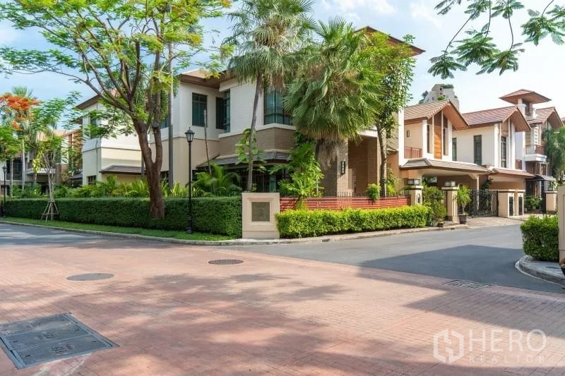 Detached House for rent in Watthana, Bangkok - Corner view of an upscale residential street with landscaped greenery and contemporary villas.