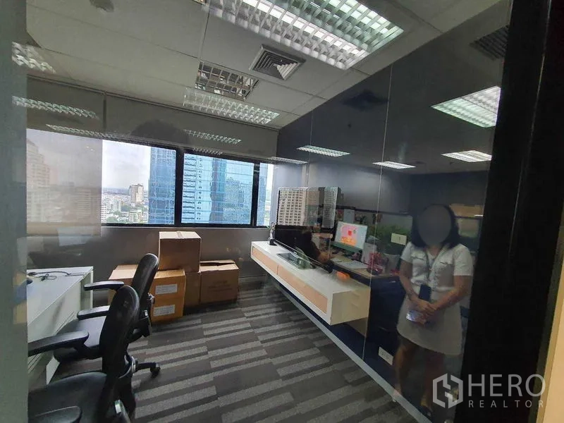 Office Space for rent in Watthana, Bangkok - Glass-walled private office with city skyline views and a built-in shelf.