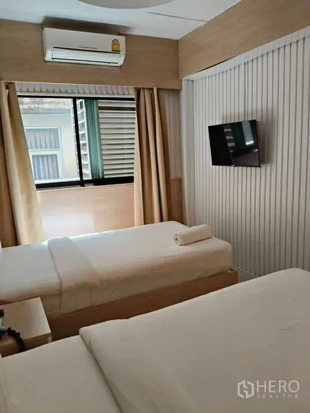 Retail Space for rent in Khlong Toei, Bangkok - Compact room with two single beds, wall-mounted TV, air conditioner and window in light wood finishes.