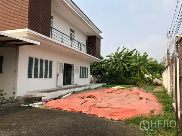 Detached House for sale in Bang Khen, Bangkok - Side view of the house showing long driveway, front yard space and banana trees along the perimeter wall.