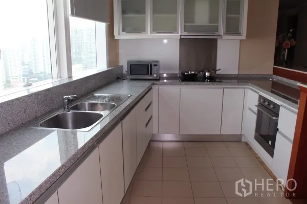 Condominium for rent in Khlong Toei, Bangkok - Modern U-shaped kitchen with granite countertops, double sink, city-view window, built-in oven and microwave.