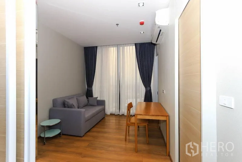 Condominium for rent in Khlong Toei, Bangkok - Secondary living or study area with sofa, writing desk and tall blackout curtains over full-height windows.