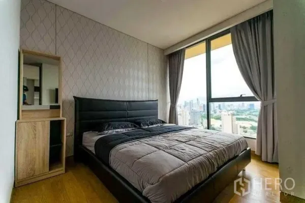 Condominium for rent in Khlong Toei, Bangkok - Cozy bedroom with large window, grey bedding and panoramic skyline view over the city.