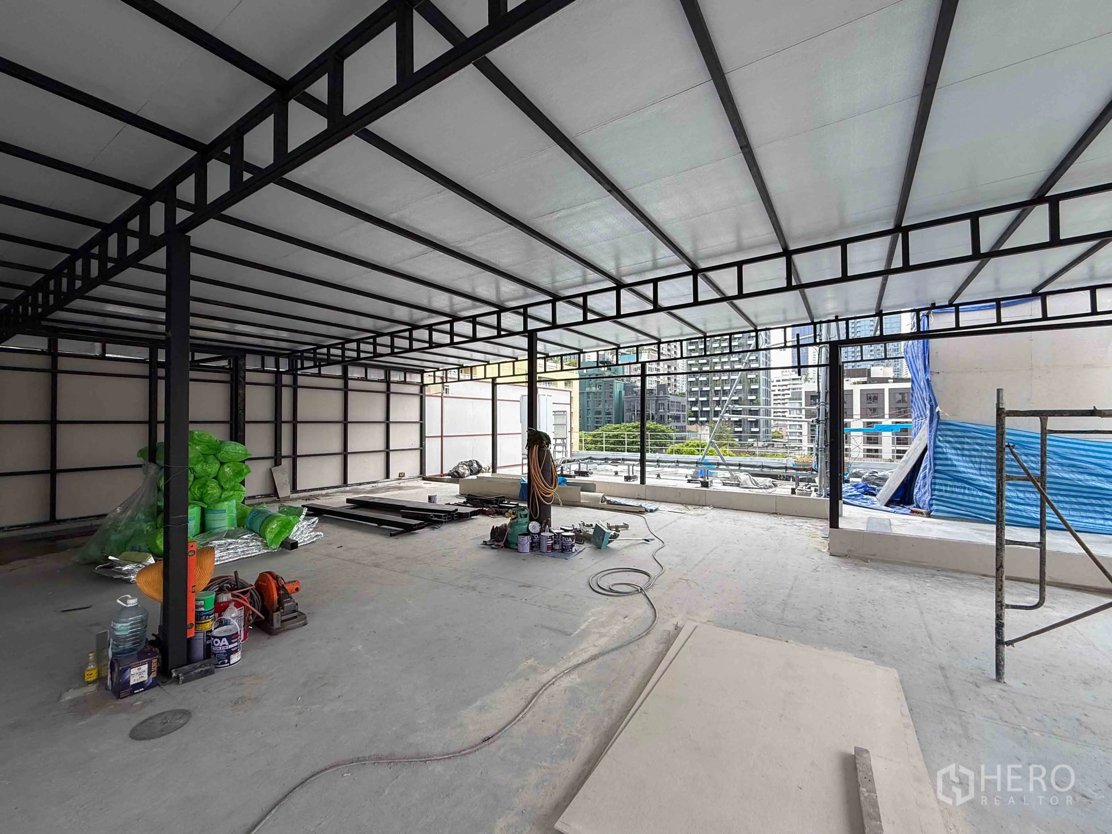 พื้นที่ขายของ for rent in Watthana, Bangkok - พื้นที่เปล่าโครงเหล็กพร้อมวัสดุก่อสร้างบนพื้น มองเห็นอาคารรอบข้าง.