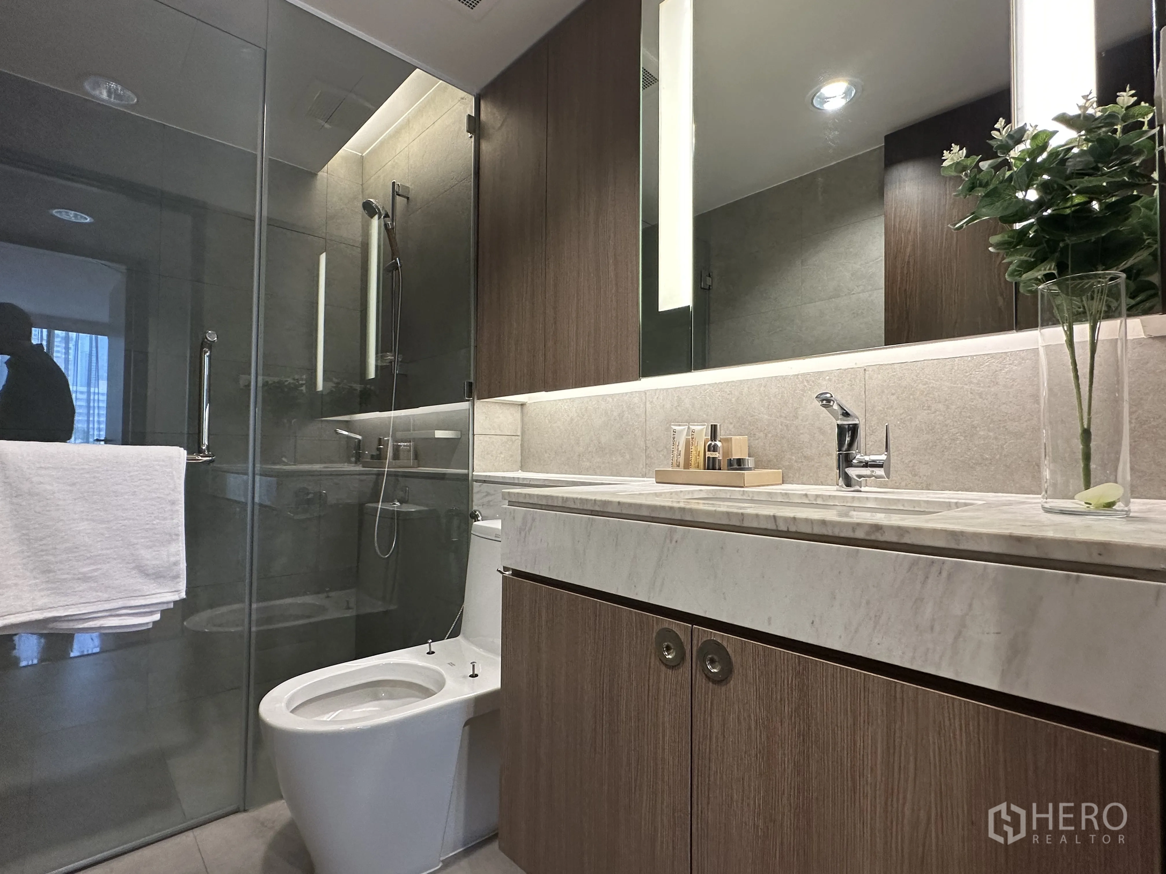 Condominium for rent in Khlong Toei, Bangkok - Sleek bathroom with glass-enclosed shower, marble countertop, and vanity storage.