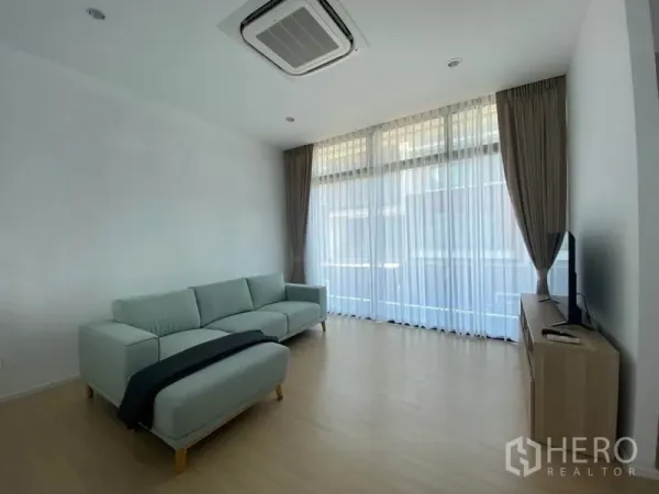 联排别墅 出租在Saphan Sung, Bangkok - 通透明亮的客厅，落地窗、嵌入式空调、沙发与电视柜。