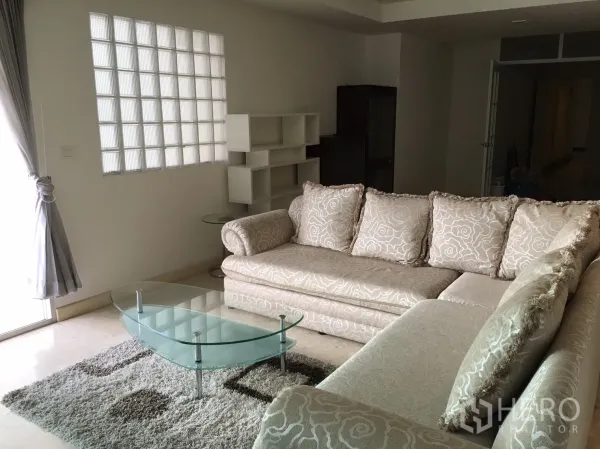 Condominium for rent or sale in Khlong Toei, Bangkok - L-shaped sofa with glass coffee table, rug and a glass-block window in the lounge.