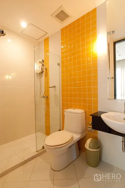 Condominium for rent in Khlong Toei, Bangkok - Second bathroom with yellow tile accent, glass shower and white ceramic fixtures.