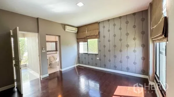 Detached House for sale in Bang Kapi, Bangkok - Bright master bedroom with wood flooring, patterned accent wall, and an en-suite bathroom.