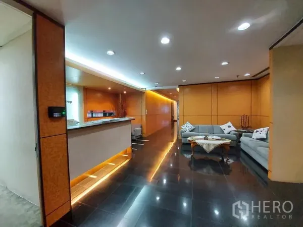 Office Space for rent in Ratchathewi, Bangkok - Reception lobby with illuminated counter, wood panel walls, grey sofas and glossy black tile flooring in a professional office building.