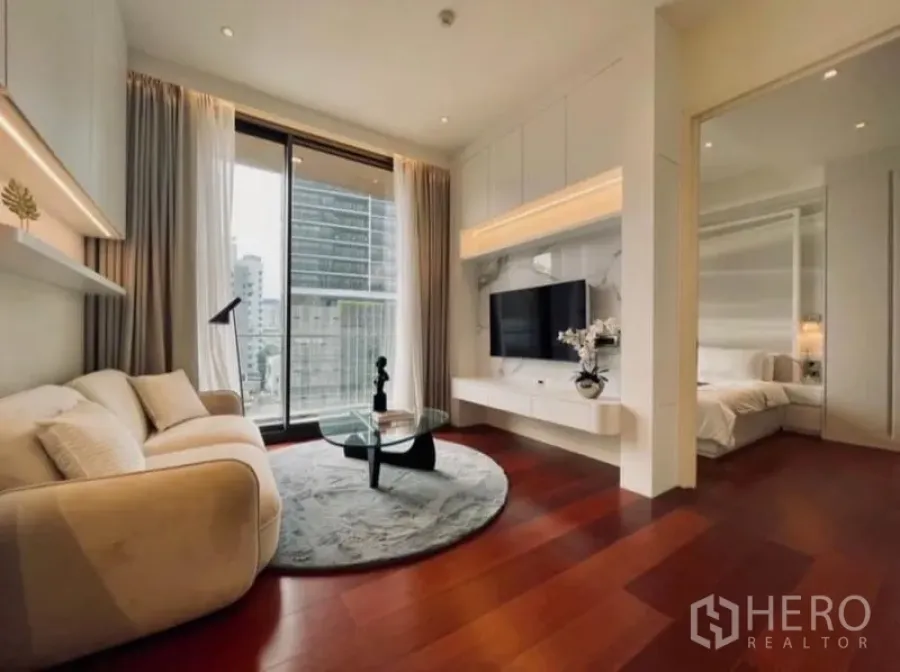 Condominium for rent in Watthana, Bangkok - Living room with city-view balcony beside doorway to serene bedroom.