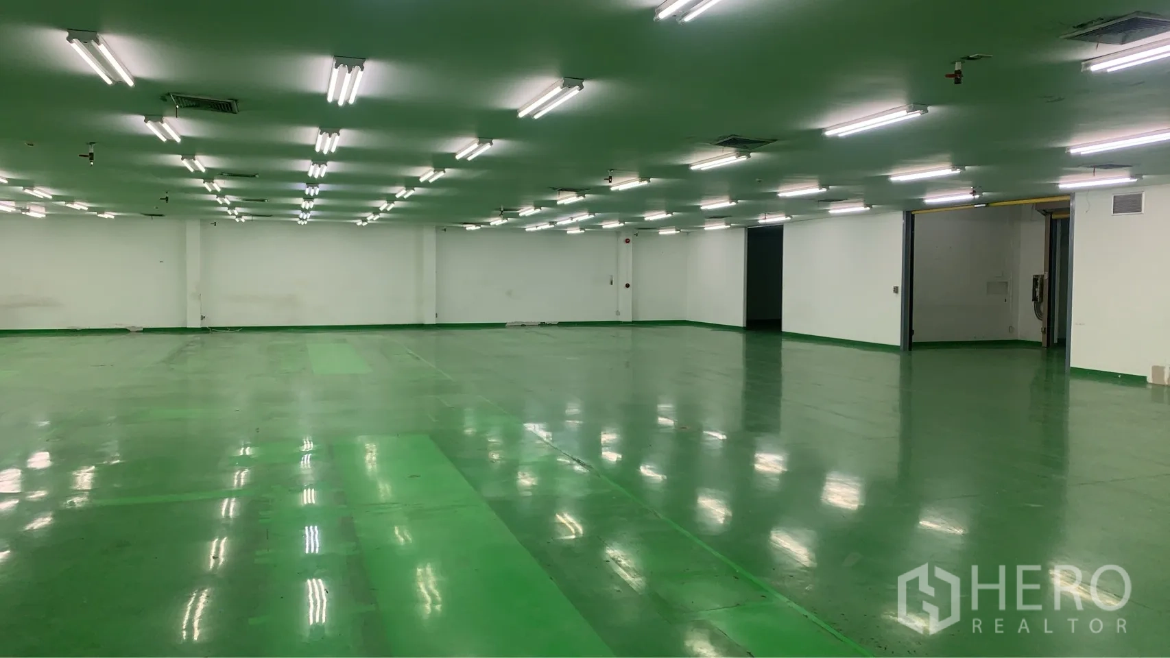 Factory for rent in Mueang Samut Prakan, Samut Prakan - Spacious workshop area with low ceiling lighting, green floor, and large openings to adjoining rooms.