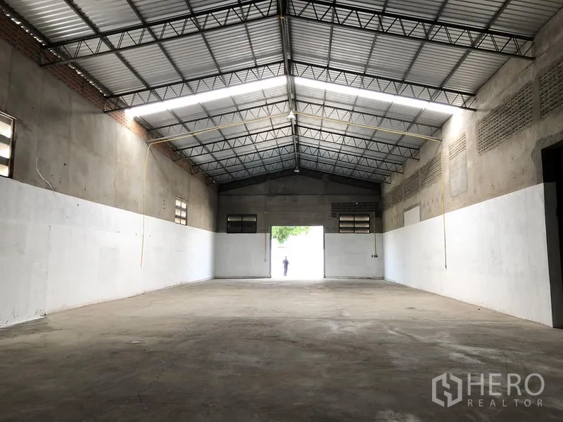 Warehouse for rent in Mueang Pathum Thani, Pathum Thani - Open warehouse hall facing the entrance, showing long LED strip lighting and smooth floor.
