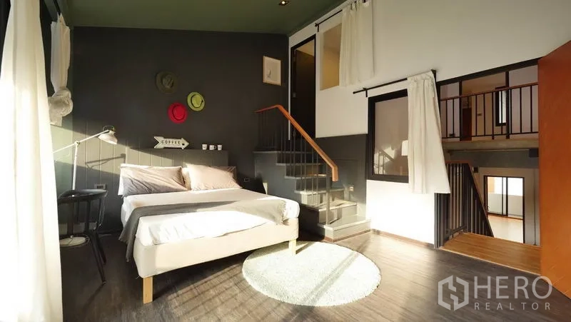 Townhouse for rent in Khlong Toei, Bangkok - Bright loft-style bedroom with mezzanine stairs, wood flooring and big windows.