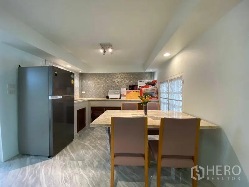 Detached House for rent in Bang Kapi, Bangkok - Kitchen-dining area with marble-top table, four chairs, stainless refrigerator, U-shaped counter, and mosaic backsplash.