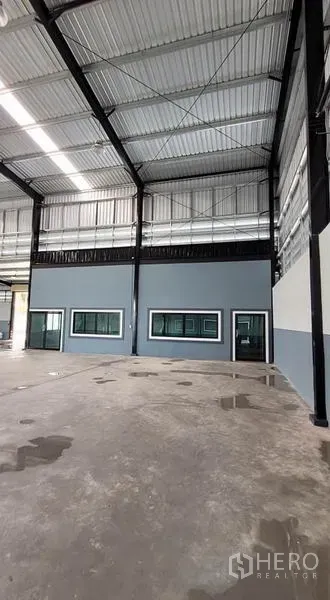 Factory for rent or sale in Phanat Nikhom, Chon Buri - Interior wall with windows and door beneath a high steel truss ceiling in the warehouse.