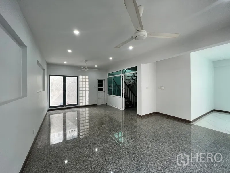 Home Office for rent in Watthana, Bangkok - Open-plan living room with glossy floors, ceiling fans and a staircase.