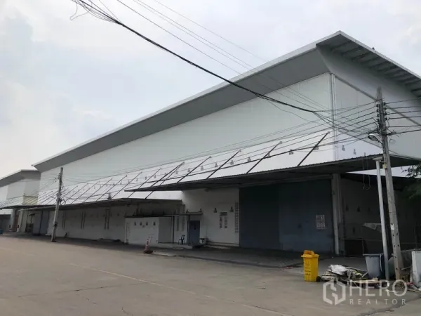 工厂 出租在Bang Bua Thong, Nonthaburi - 现代白色工厂外立面，沿道路设有长条形装卸雨棚。