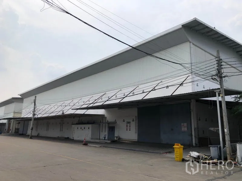 工厂 出租在Bang Bua Thong, Nonthaburi - 现代白色工厂外立面，沿道路设有长条形装卸雨棚。