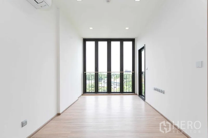 Condominium for sale in Watthana, Bangkok - Bright living area with tall balcony doors and green neighborhood view.