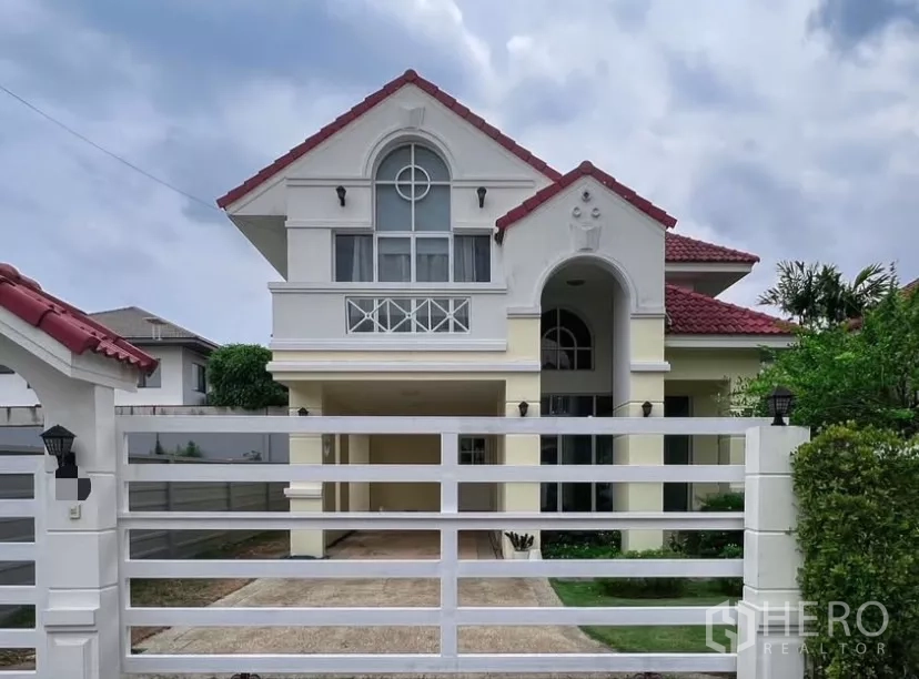 Detached House for rent or sale in Prawet, Bangkok - Front elevation behind a white gate showing arched porch and covered carport.