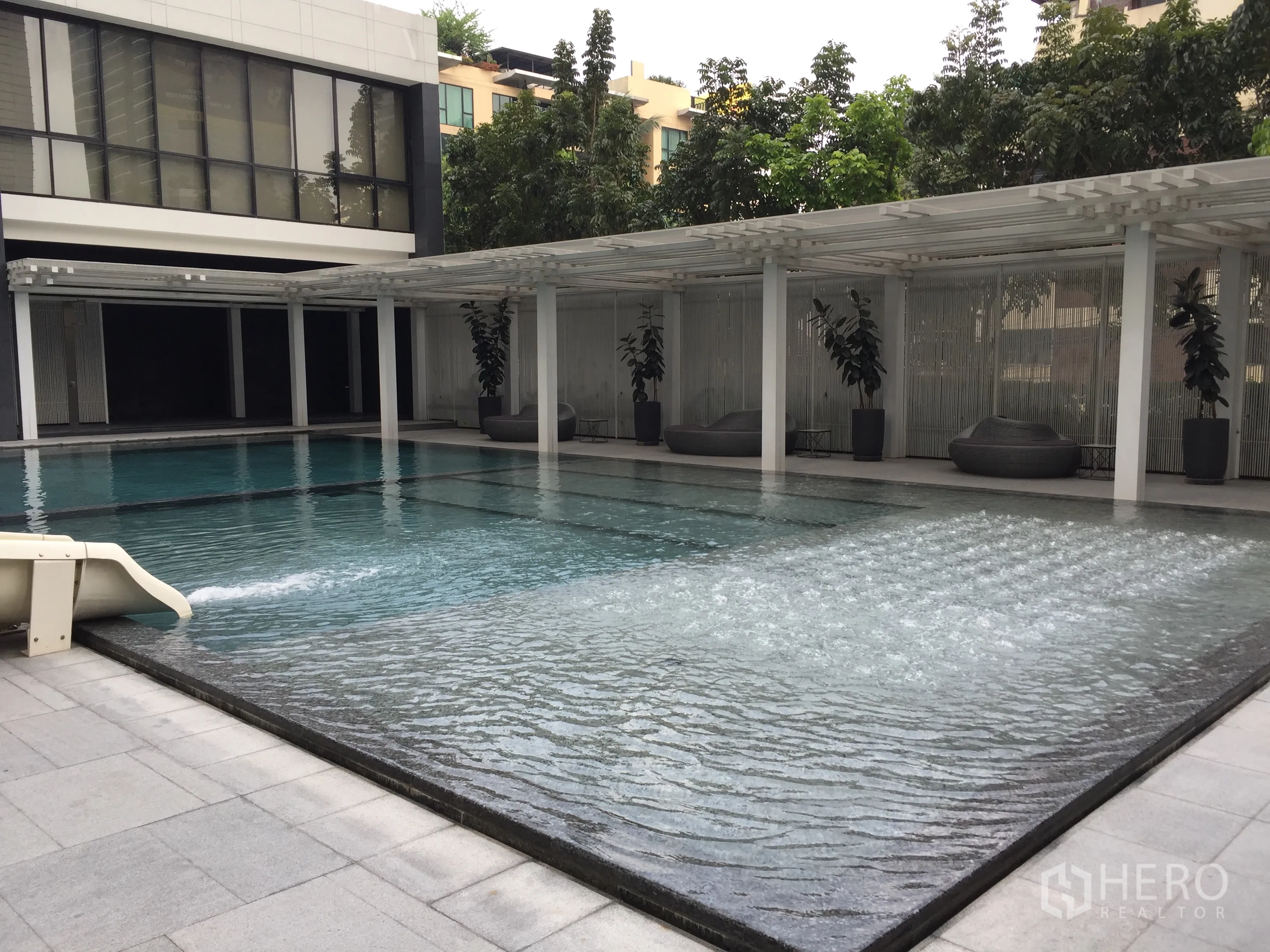 Condominium for rent in Pathum Wan, Bangkok - Outdoor swimming pool with shallow sun shelf, pergola shade and greenery around.
