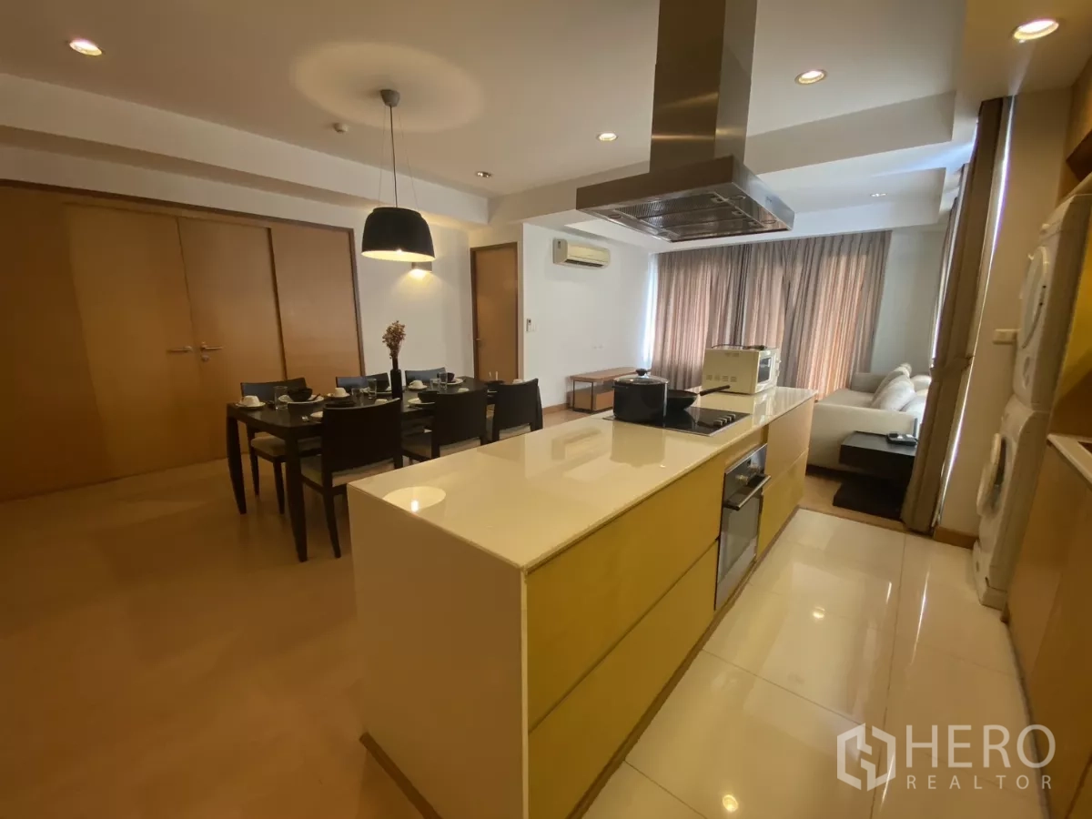 Condominium for rent in Watthana, Bangkok - Sleek kitchen island with cooktop and hood facing the dining table and sofa in an open-plan layout.