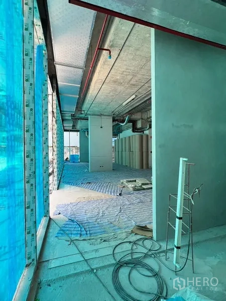 Retail Space for rent in Khlong Toei, Bangkok - Entry corridor of the retail unit showing exposed MEP services and blue protective film on windows.