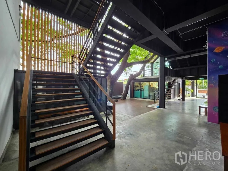 Home Office for rent in Chatuchak, Bangkok - Airy atrium with broad staircase, mature tree integrated into the design, and glass-walled rooms.