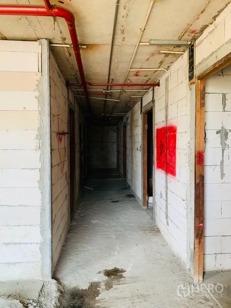 Home Office for rent - Long concrete hallway under construction with red sprinkler pipes and block walls.