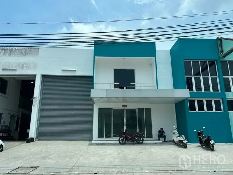 工厂 出租或出售在Samut Prakan - 邦普利现代工厂外观，青绿色立面、玻璃门厅与大型卷闸装卸门。