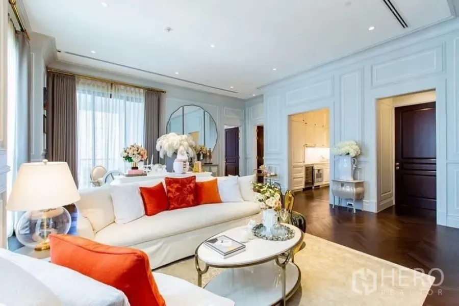 Condominium for sale in Pathum Wan, Bangkok - Bright living room with classic wall paneling, white sofa and orange cushions in a luxury Pathum Wan condo.