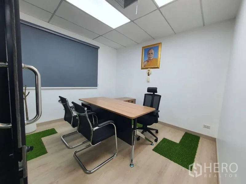 Office Space for rent - Private executive office with desk, guest chairs, roller blind and small green carpet patches.