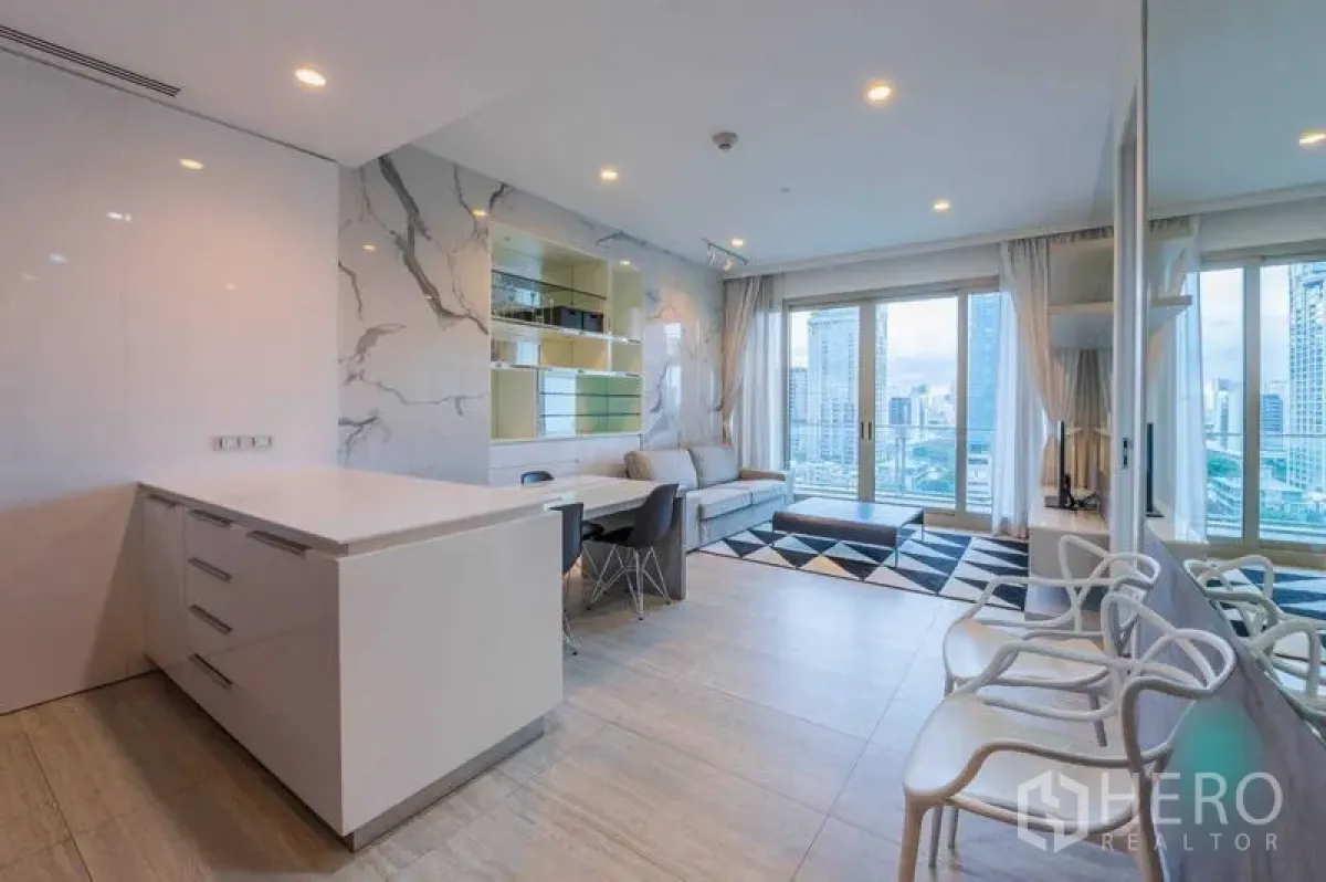 Condominium for rent in Pathum Wan, Bangkok - Spacious open-plan living with island counter, wall shelving, sliding doors to the balcony, and a mirrored feature wall.