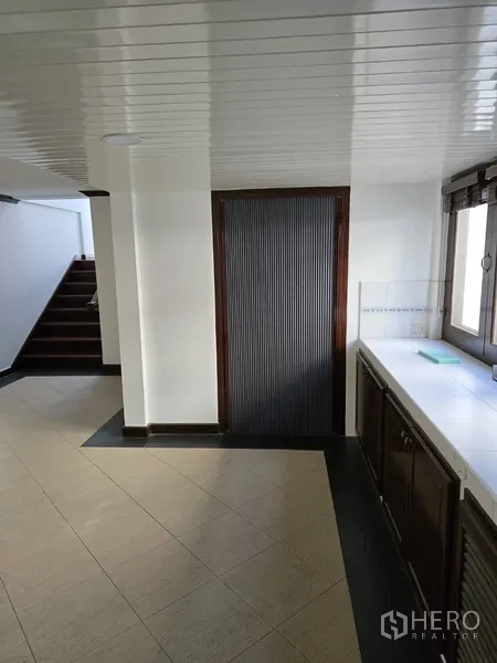Detached House for rent in Watthana, Bangkok - Kitchen corridor beside stairs with dark slatted door and counter.