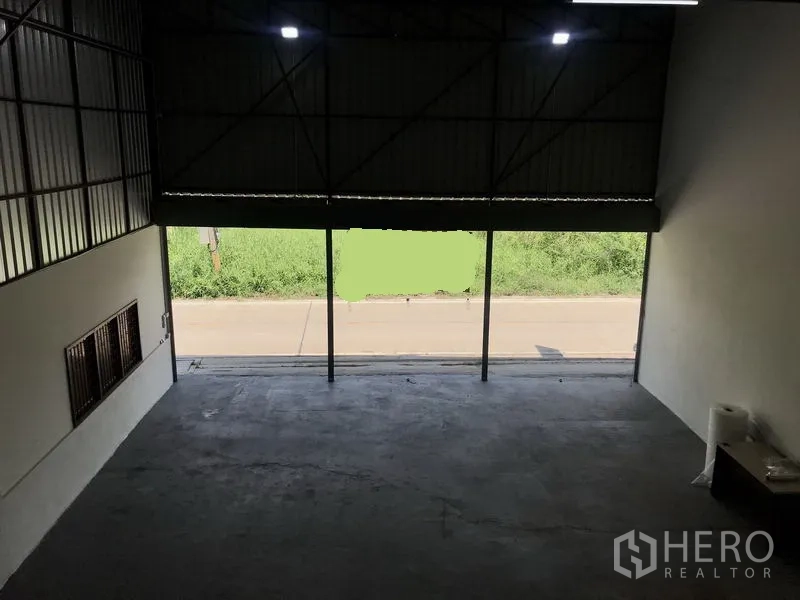 Warehouse for rent in Lam Luk Ka, Pathum Thani - View from the mezzanine toward a large roller door opening to the road and green verge.
