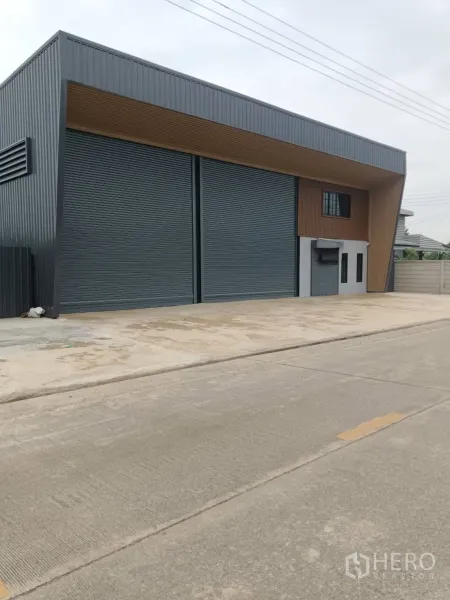 Warehouse for rent in Lam Luk Ka, Pathum Thani - Angled street view of the warehouse frontage with spacious driveway for vehicle access.