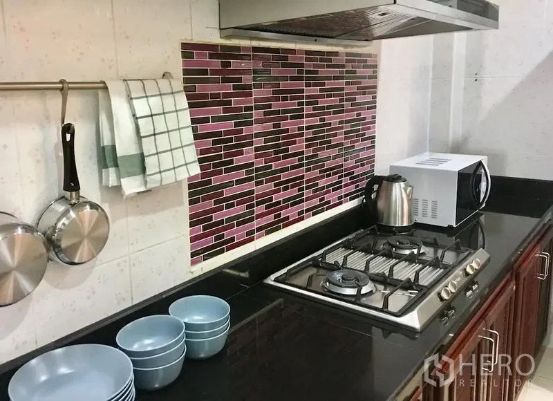 Townhouse for rent in Bang Rak, Bangkok - Kitchen close-up showing gas hob, stainless hood, black granite countertop, mosaic backsplash, kettle and microwave.